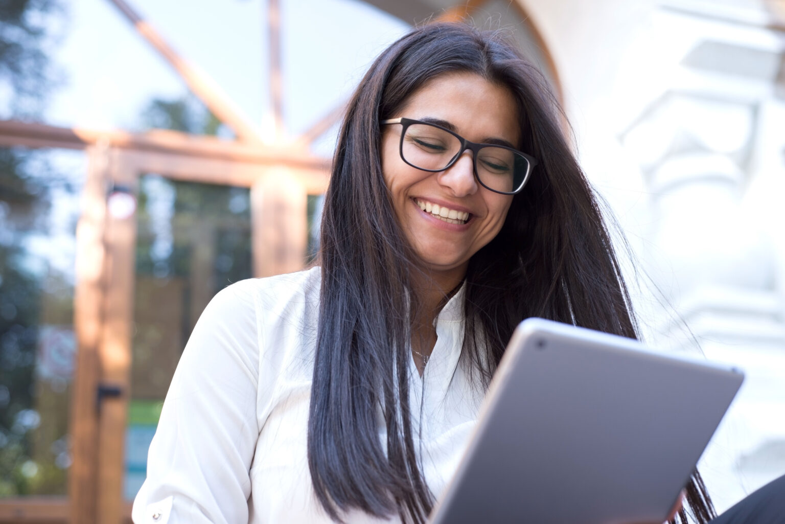 Portrait of a beautiful indian girl. Business woman, wearing glasses, smiling, sitting on the steps of an office building, holding a tablet in her hand